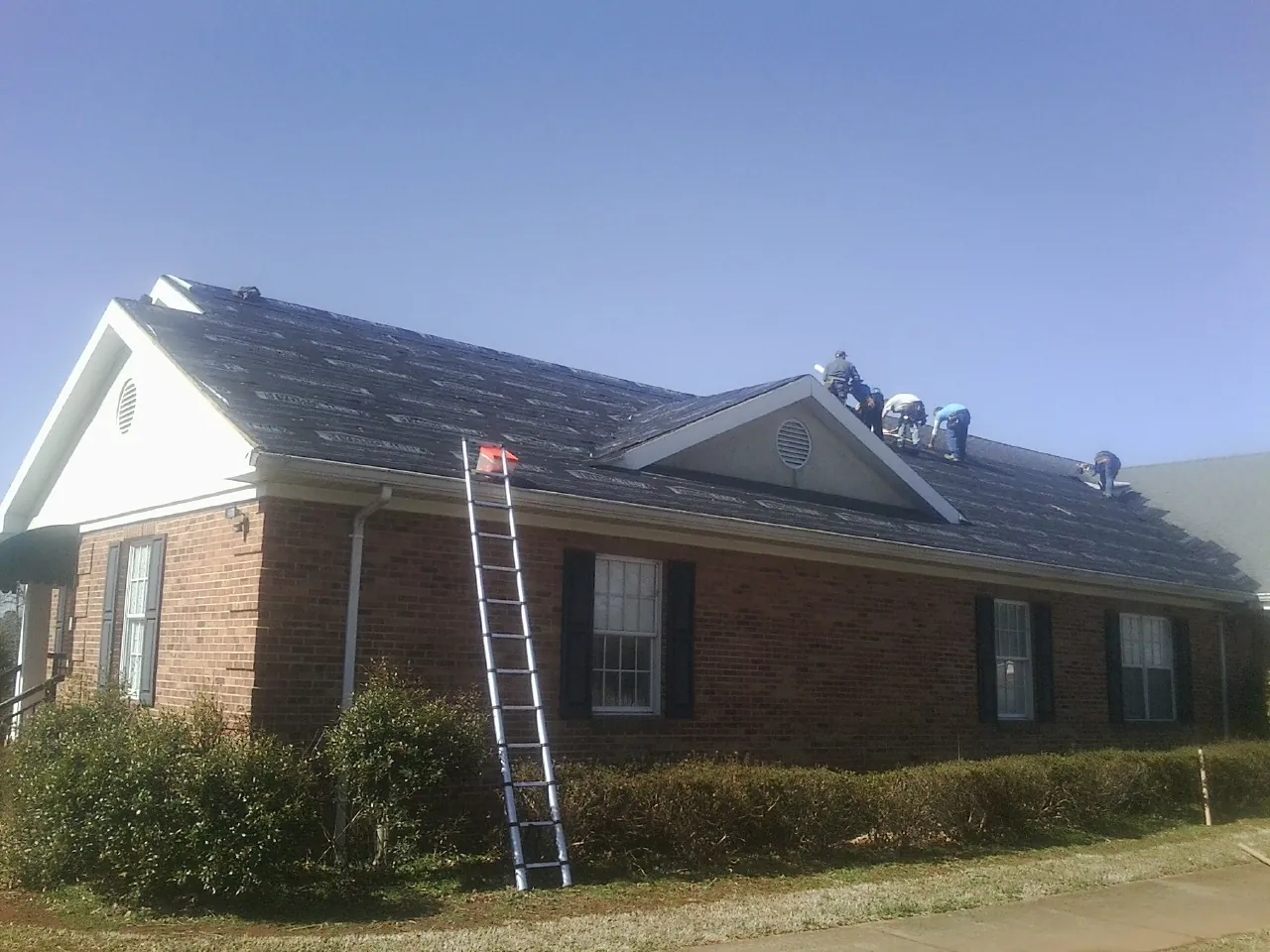 Crew tearing shingles off a brick ranch roof with a ladder set — Emergency Roof Repair work by our crew in Rock Falls