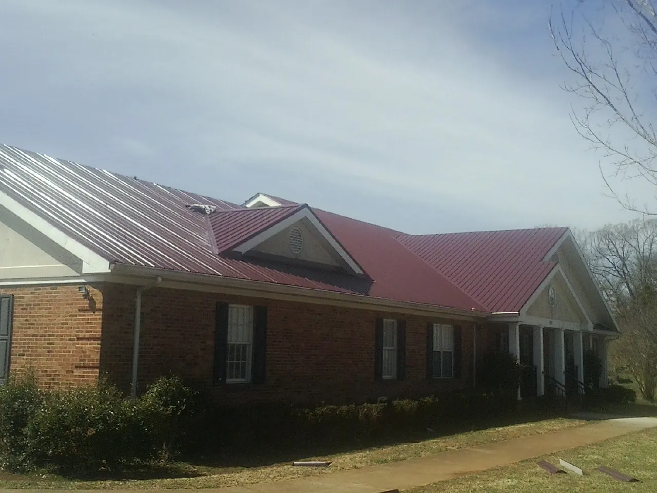 Red metal roof with gabled entries on a long brick building, from a Hail Damage Roof Repair job in Rock Falls