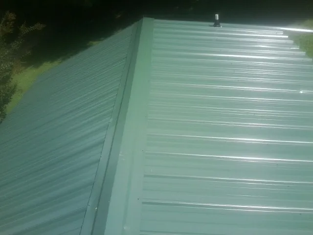 New green metal panels meeting at the ridge of a roof — Flat Roof Repair work by our crew in Rock Falls
