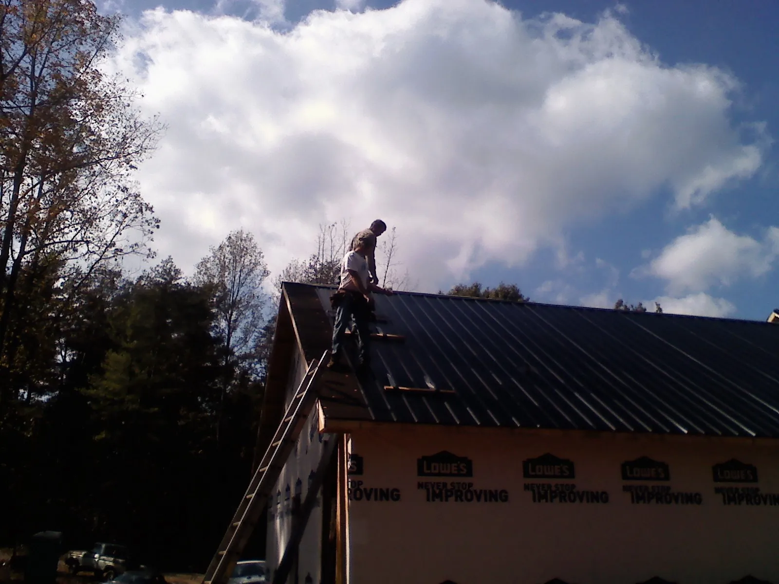 Roofer fastening dark metal panels high against a cloudy sky, from a Roof Inspection job in Rock Falls