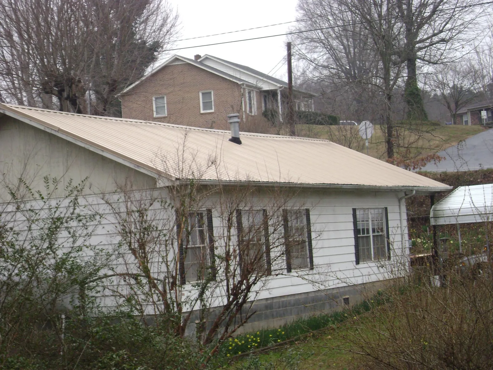 Tan metal roof on a white sided house set into a hillside — Commercial Roofing by Roofing Brothers in Rock Falls